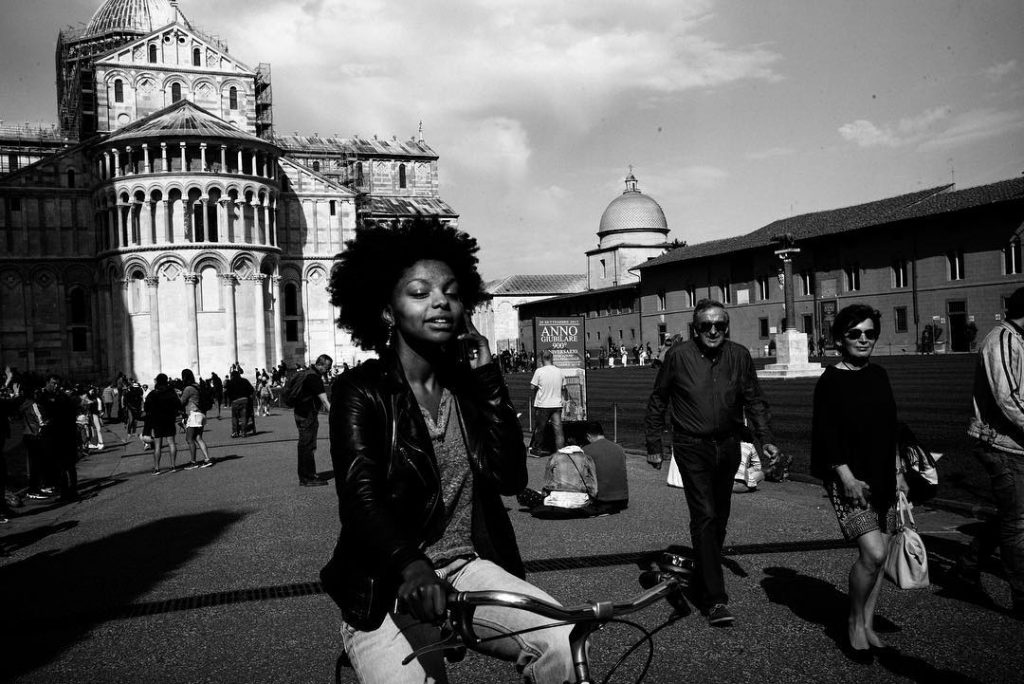 Girl biking around Pisa while talking on the phone. Around her, people are walking, talking and looking at the monuments.
